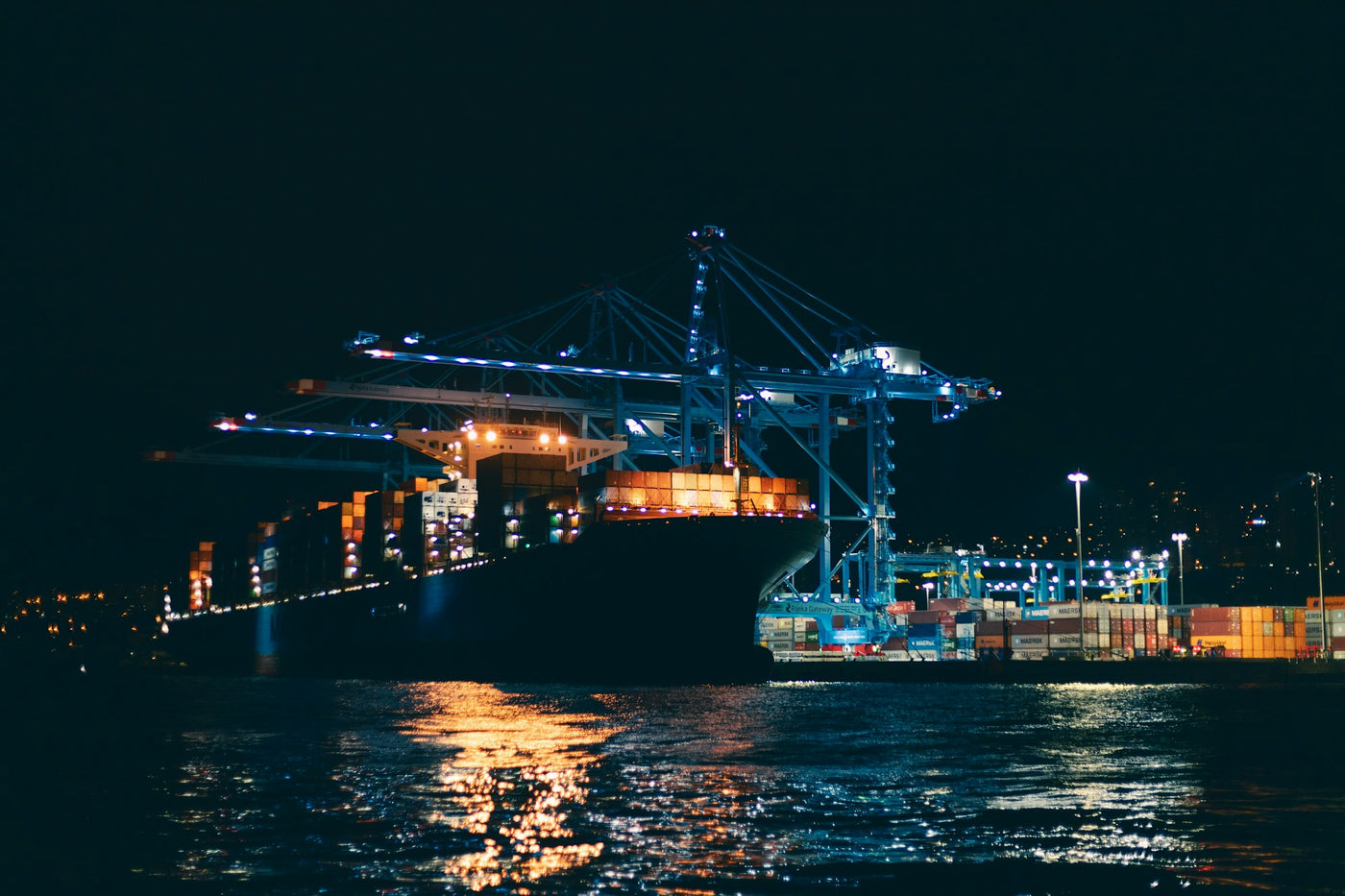 Cargo ship at a brightly lit container port at night — global logistics